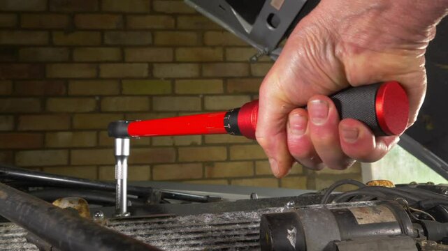 Closeup of a man&rsquo;s hand in the engine bay of a vehicle in a garage, turning a torque wrench tool on a nut or bolt, to tighten to the correct tension.