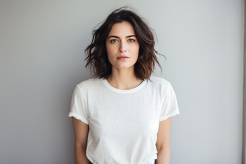 Obraz premium Portrait of a content woman in her 30s dressed in a casual t-shirt in minimalist or empty room background