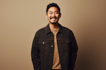 Obraz premium Portrait of a satisfied asian man in his 30s sporting a rugged denim jacket while standing against minimalist or empty room background