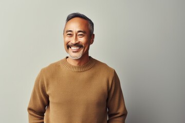 Obraz premium Portrait of a happy asian man in his 50s wearing a cozy sweater while standing against minimalist or empty room background