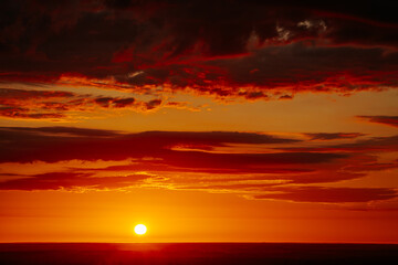 A radiant sunset over a forested horizon, with the sun casting a warm, golden glow across the sky...