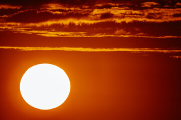 A close-up view of the intense sunset with a vibrant orange sky. The sun is prominently featured, casting a warm glow and illuminating the clouds.
