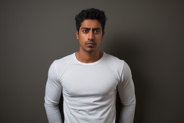 Obraz premium Portrait of a glad indian man in his 20s sporting a long-sleeved thermal undershirt on minimalist or empty room background