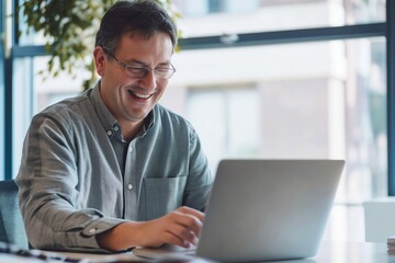 Fototapeta premium A man is sitting at a desk with a laptop in front of him. He is smiling and he is enjoying himself