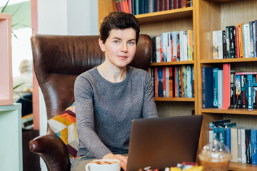 Confident middle aged female expert sits with laptop in leather armchair in cozy office with...