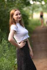 Portrait of a beautiful long-haired girl in a white T-shirt and black skirt in a city park.