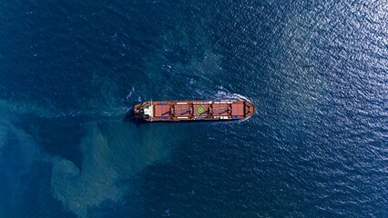 Aerial top view large general cargo ship bulk carrier running hi-speed in the deep sea.