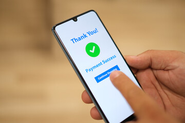 The male hand holding a cell phone with the payment app interface showing the payment successful message with a green check mark. Online shopping, mobile banking and transactions.