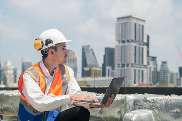 A male engineer works with communications on the roof of a tall building with surrounding engineering systems.