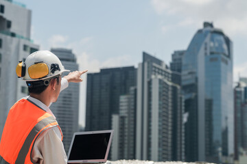 A male engineer works with communications on the roof of a tall building with surrounding engineering systems.