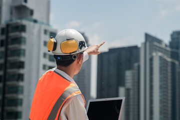 A male engineer works with communications on the roof of a tall building with surrounding engineering systems.