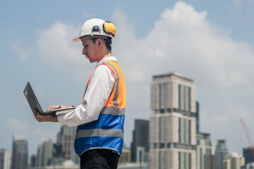 A male engineer works with communications on the roof of a tall building with surrounding engineering systems.