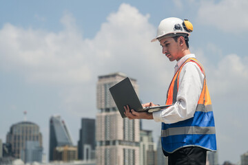 A male engineer works with communications on the roof of a tall building with surrounding engineering systems.
