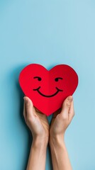 Obraz premium Hands holding a smiling red heart on a blue background