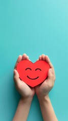 Fototapeta premium Hands holding a red heart with a smiley face on a turquoise background