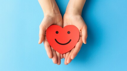 Obraz premium Hands holding a smiling heart on blue background symbolizing love, care, and happiness