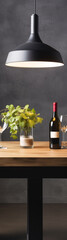 Black background with a wooden table with a lamp hanging over it, a vase of green leaves, a bottle of red wine and two wine glasses.