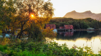 Sunset sun over red fishing cabins and boats by fjord in the costal village of Helgeland . Foroy, Norway