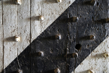 Detail of a white, black painted fortified centuries-old fortress door with diagonal lines and protruding iron points. Intended as white black grunge background