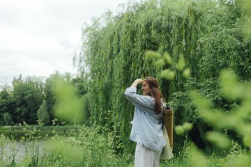 Korean girl with yoga mat for practicing yoga looking for a place to meditate in the park. Unity with nature and self sufficient concept. Part of the series.