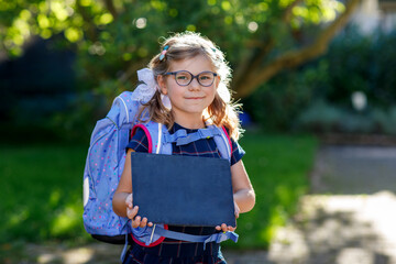 Happy little kid girl with eye glasses with backpack or satchel and big school bag on the first day...