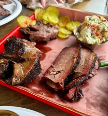 Texas beef barbecue on red platter with brisket, ribs, potato salad and pickles