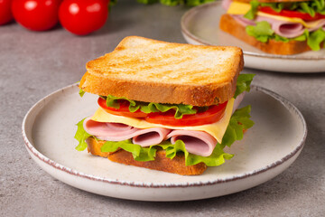 Close-up of two sandwiches with bacon, salami, prosciutto and fresh vegetables on rustic wooden cutting board. Club sandwich concept