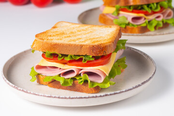 Close-up of two sandwiches with bacon, salami, prosciutto and fresh vegetables on rustic wooden cutting board. Club sandwich concept