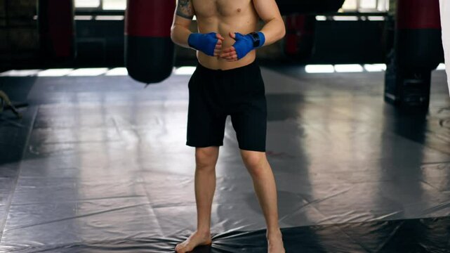 in a boxing fight club bald young boxer with tattoos in blue bandages trains a kick before a fight professional training fighting technique training