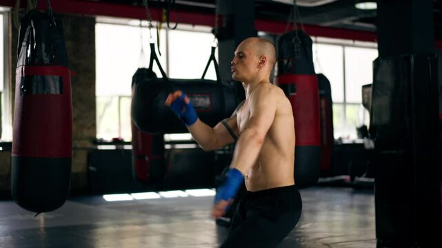 in a boxing fight club bald young boxer with tattoos in blue bandages trains a kick before a fight professional training fighting technique training