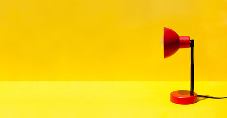 Red lamp on table in room with copy space. A red lamp on a bright yellow background. Minimal office or school equipment. Back to school, back to office concept. Minimal template concept. Banner