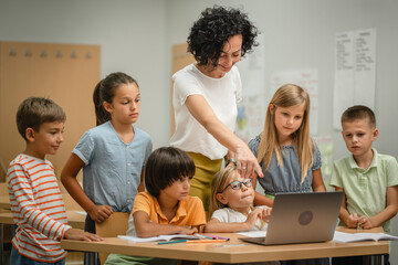 Mature teacher teach her students how to use laptop in the classroom
