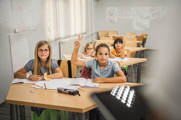 Young girl student raise his hand to answer a question during a lesson