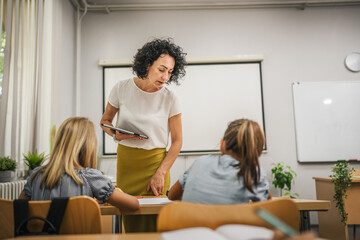 Mature teacher hold tablet and check how her students learn lesson