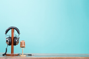 Golden microphone and retro headphones standing on wooden table front mint blue background. Vintage style filtered photo