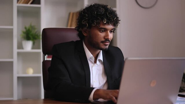Portrait of young handsome indian  businessman thinks questioningly finding solution and typing on laptop computer at office workplace Idea pointing forward index finger concept