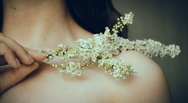 a woman holds a flower near her collarbone