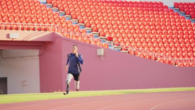 Slow motion with front view of sport man athlete prosthesis legs is jogging on track in the stadium to practice with warm light in evening.
