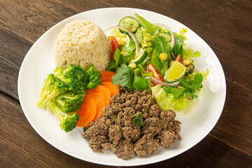 A colorful plate featuring ground beef, steamed broccoli, fresh carrots, brown rice, and a mixed green salad with lime wedges.