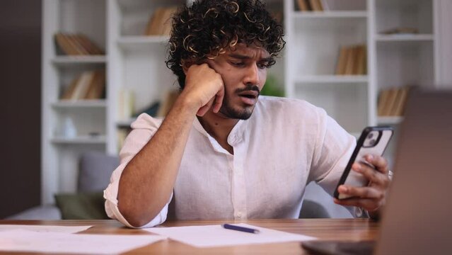 Boring young indian man scrolling feed of social networks products in internet store on smartphone while take a break indoors Tired exhausted female look at screen without enthusiasm at home workplace