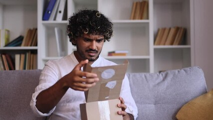  Handsome man received parcel dissatisfied with shopping in online internet store at home Upset guy customer disappointed looking at box with purchase order while open carton indoors