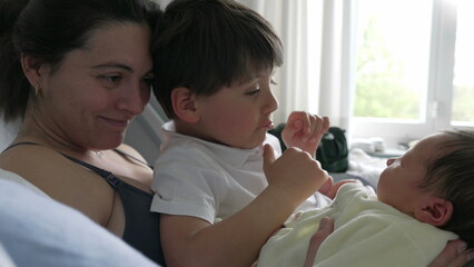 Mother and older sibling gently admiring newborn baby in hospital bed. family moment emphasizes the warmth and connection between siblings and the loving care of the mother