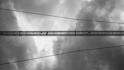 Sky Bridge 721 in Dolni Morava, Czech Republic, the worlds longest suspension footbridge. Seen in black and white from below, with people walking and intricate cables visible.