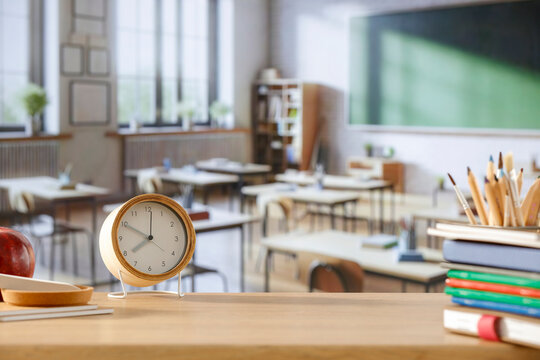 School desk and alarm clock and copy space for product in a big bright classroom interior.