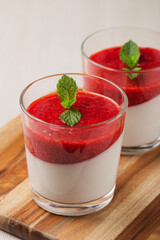 Close up coconut Panna cotta with strawberry sauce in glasses on white wooden table. Healthy dessert. Vegan food. Vertical orientation.
