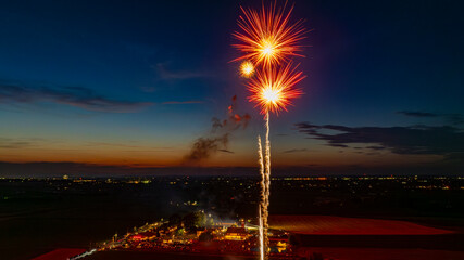 Bright Fireworks Exploding In The Evening Sky, Illuminating The Twilight Horizon, With City Lights...