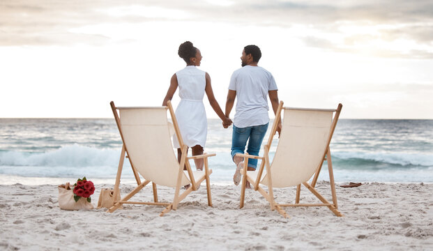 Sunset, black couple and break with beach chair, holding hands or celebrating for anniversary. Vacation, picnic and people travel for marriage on honeymoon, summer holiday and happy bonding in Miami