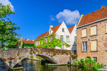 Fototapeta premium Peerdenbrug stone bridge across Groenerei Green Canal water of Reie river with plants, Brugge old town district, medieval houses buildings in Bruges city historical centre, Flemish Region, Belgium