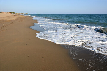 A wide empty sea beach on which foamy waves are rolling. Summer tourist landscape