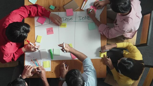 Top view of people writing and making scrum task board while writing marketing and planning strategy at colorful sticky notes. Smart team manage work performance by using kanaban board. Convocation.